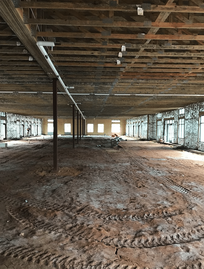 Large commercial construction interior showing exposed soil floor and mold growth on walls with no vapor barrier installed — Charlotte NC